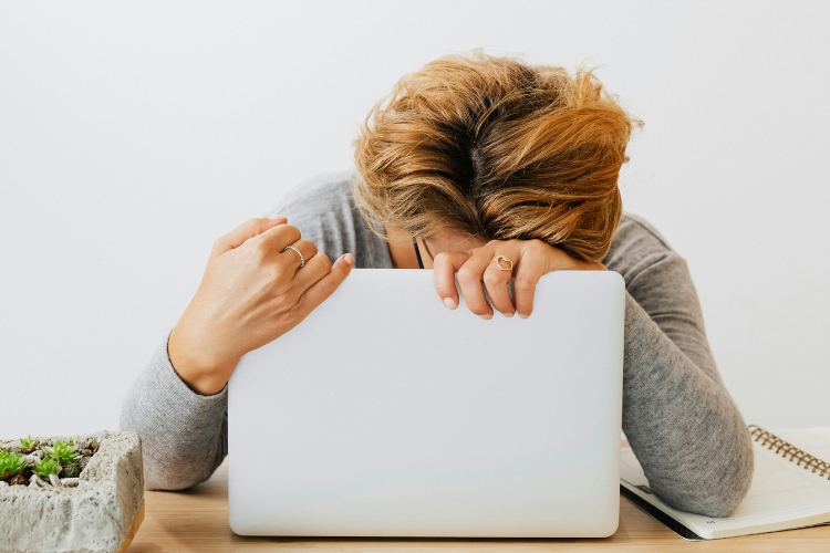 Emotionally exhausted woman leaning on laptop.