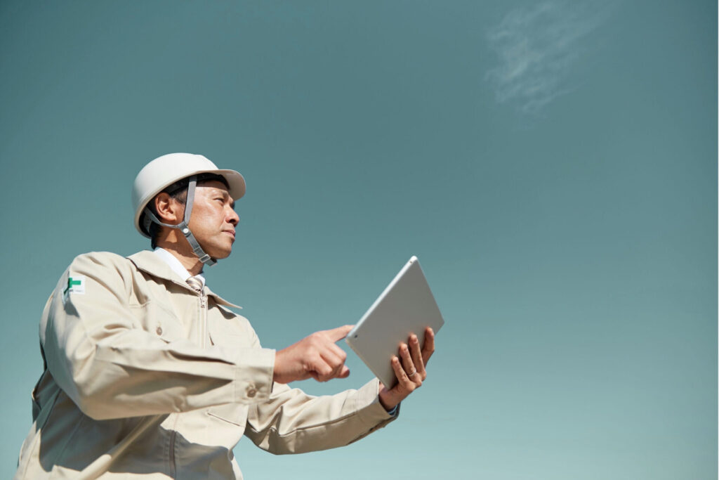 An image of a work supervisor holding a tablet and looking upwards towards the sky.